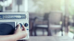 Microfone de rádio em um estúdio simples, com pessoas ouvindo ao fundo, simbolizando a voz de uma rádio comunitária